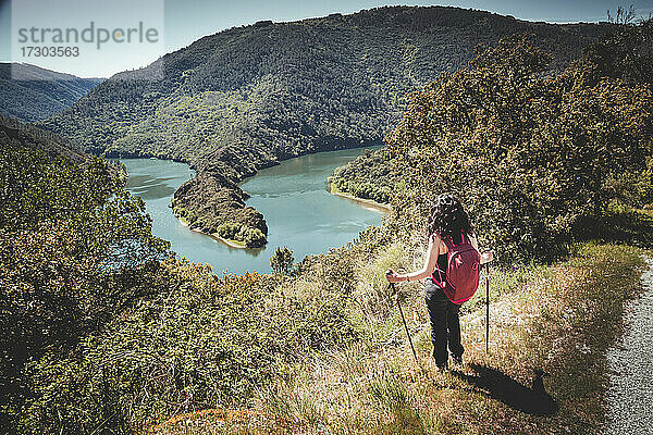 Frau mit Rucksack auf dem Gipfel eines Berges mit Blick auf den Fluss