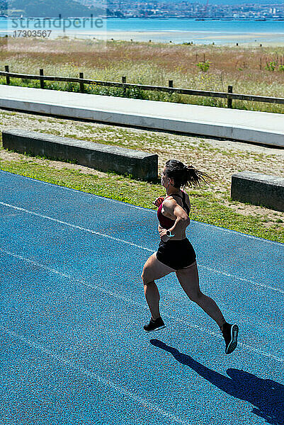 Rückenansicht einer jungen Sprinterin beim Laufen auf einer Leichtathletikbahn