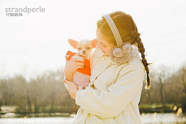 Porträt eines glücklichen Teenager-Mädchens mit ihrem kleinen Chihuahua-Hund. Ein Mädchen auf dem Hintergrund der Natur umarmt ihren Chihuahua-Hund in der Kleidung.