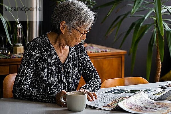 Ältere Frau liest Zeitung und sitzt mit Kaffee am Tisch