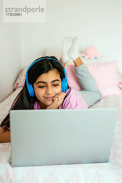 Fröhlicher Teenager  der im Bett einen Laptop benutzt und Musik hört