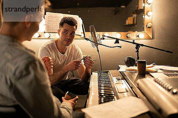Mann im Gespräch mit einem Kollegen in der Nähe des Digitalpianos während einer Pause im Aufnahmestudio