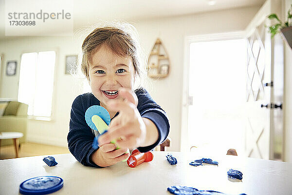 Porträt eines fröhlichen Mädchens  das zu Hause auf dem Tisch mit Spielzeug spielt