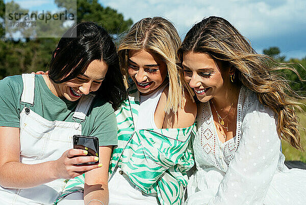 Drei Freundinnen benutzen ein Mobiltelefon und haben Spaß