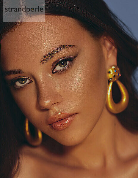 Schöne Frau glatte lange Haare brunette Abend Make-up mit Liner gebräunte Haut schöne weibliche Porträt über blauen Hintergrund tragen goldene Ohrringe