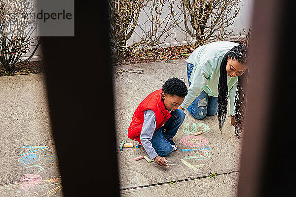 Mutter und Sohn haben Spaß daran  gemeinsam Kreide auf Beton im Hinterhof zu benutzen