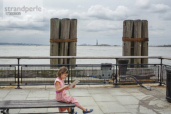 Ein kleines Kind sitzt auf einer Bank am Hudson mit Blick auf die Freiheitsstatue