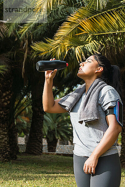 junge Sportlerin  die im Park aus einer Flasche trinkt