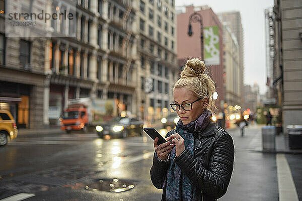 Attraktive Frau benutzt ihr Smartphone auf einer belebten städtischen Straße