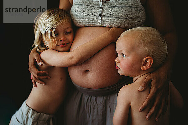 Schöne blonde Kinder umarmen Mamas schwangeren großen Bauch zu Hause