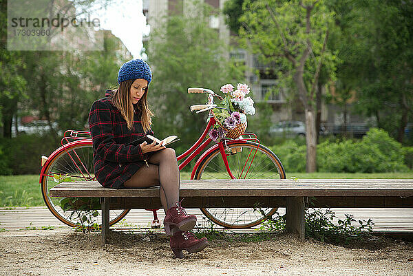 Eine Frau liest ein Buch  ein rotes Fahrrad und ein Korb mit bunten Blumen.