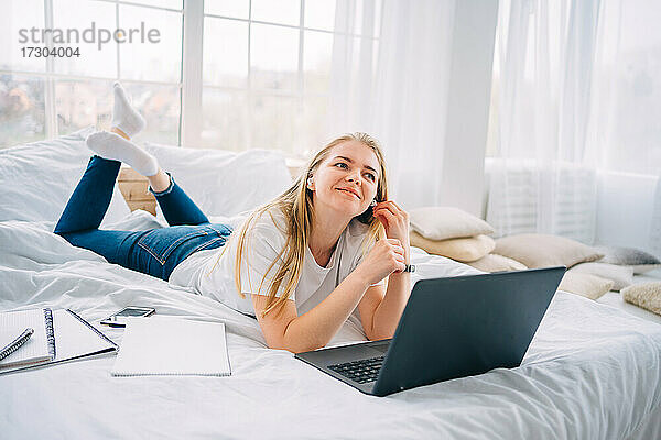 Blondes Mädchen arbeitet am Laptop im Bett