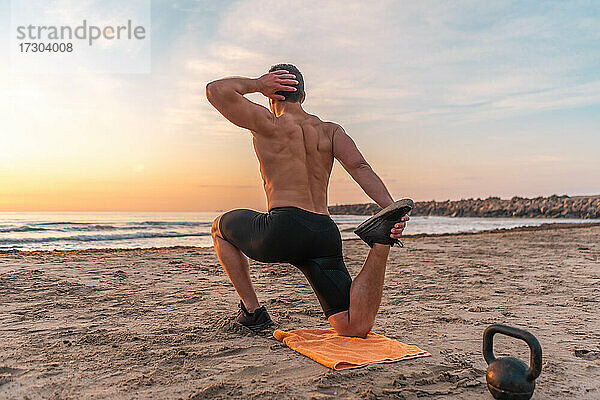 muskulöser Mann beim Training am Strand bei Sonnenaufgang