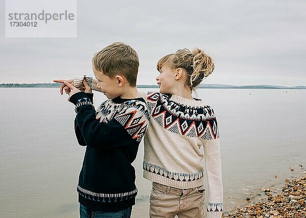 Bruder und Schwester spielen zusammen am Strand und zeigen auf das Meer