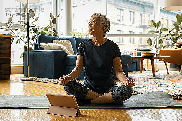 Ältere Frau meditiert  während sie zu Hause über ein digitales Tablet lernt