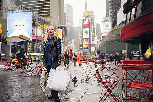 Positive Frau mit Einkaufstüten auf dem verregneten Times Square