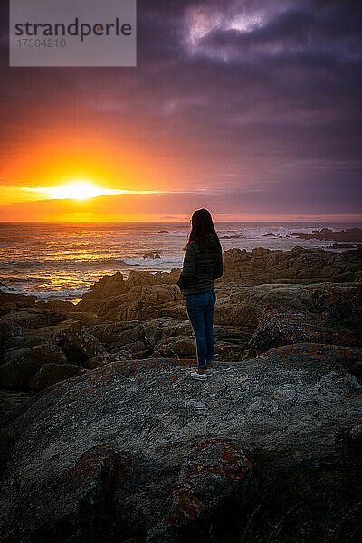 Frau beobachtet einen schönen Sonnenuntergang Felsen Strand friedliche Landschaft