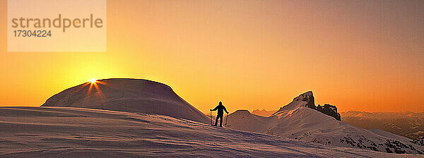 Panoramablick auf einen Forscher auf einem verschneiten Bergkamm bei Sonnenuntergang.
