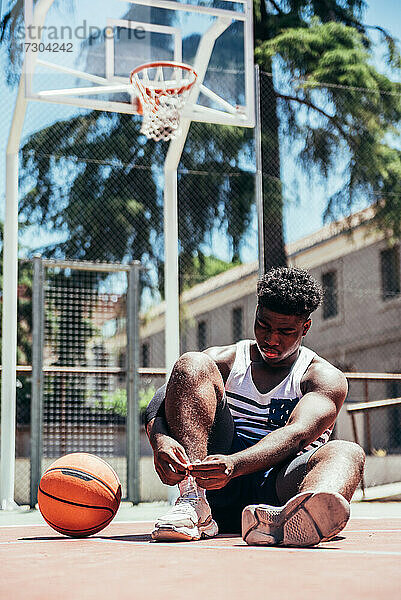 Porträt eines schwarzen afroamerikanischen Jungen  der seine Schnürsenkel auf einem städtischen Basketballplatz bindet.