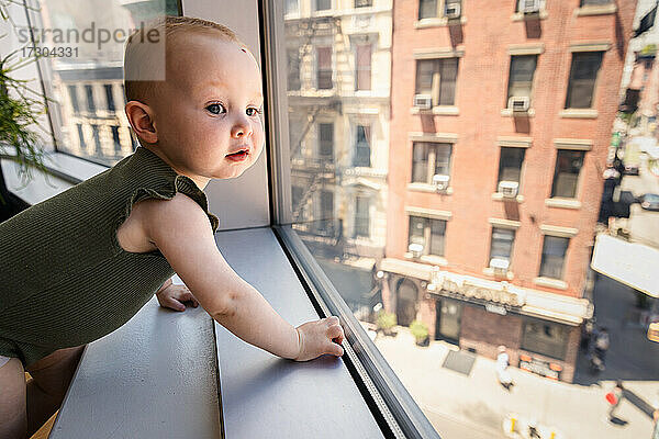 Neugierige glückliches Baby Mädchen schaut aus dem Fenster in der Stadt