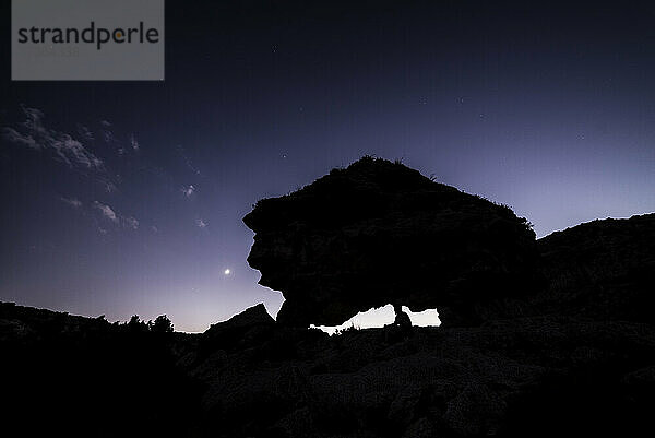 Mann sitzt auf einem neolithischen Dolmen und genießt den Sonnenuntergang