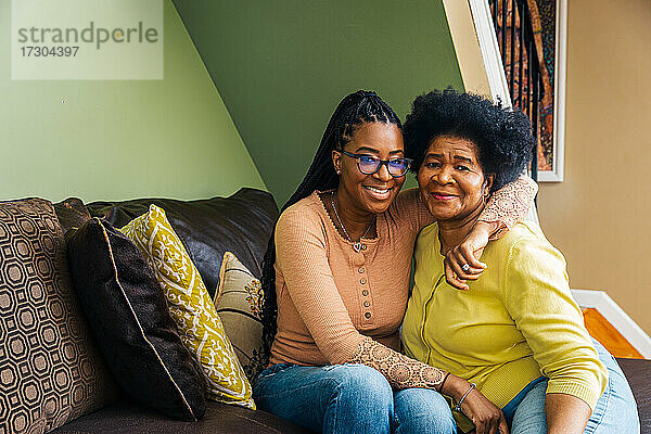 Porträt einer lächelnden älteren Frau mit Tochter  die zu Hause auf dem Sofa sitzt