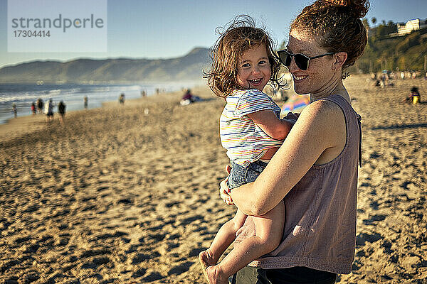 Seitenansicht einer glücklichen Mutter mit ihrer Tochter am Strand während eines Wochenendes