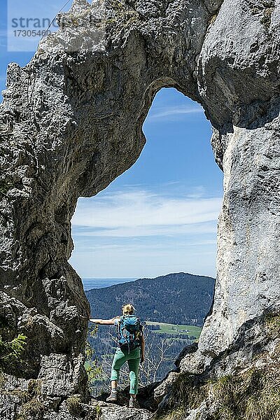 Wanderin steht im Felsentor Breitensteinfensterl mit Ausblick auf Hochnebel über dem Tal  Wanderweg zum Breitenstein  Fischbachau  Bayern  Deutschland  Europa