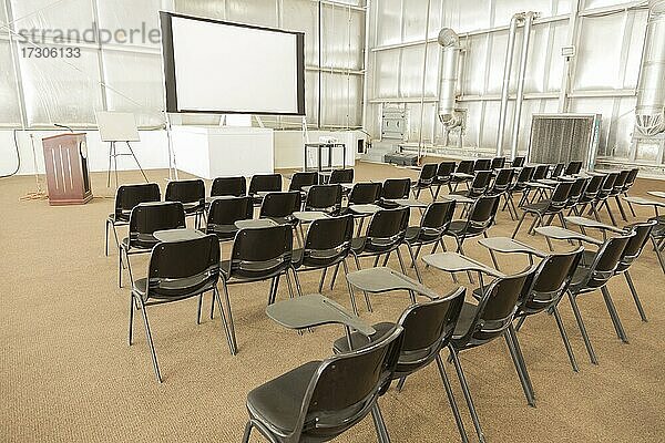 Leerer Präsentationskonferenzraum mit Schreibtischstühlen und Projektorleinwand