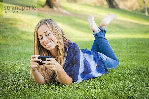 Lächelnde junge Frau mit Handy im Freien im Park