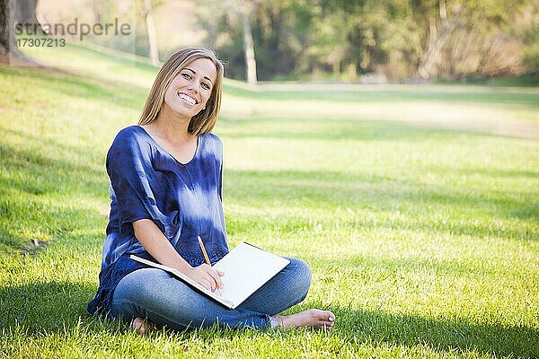 Porträt einer schönen jungen Frau mit Buch im Freien im Park