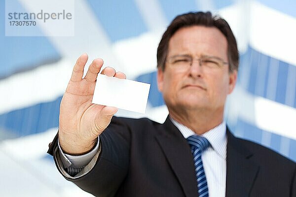 Gutaussehender Geschäftsmann in Anzug und Krawatte hält eine leere Visitenkarte vor einem Firmengebäude