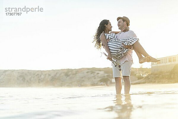 Ein junger Mann trägt seine geliebte Frau am Strand bei Sonnenuntergang an der Algarve  Portugal  Europa