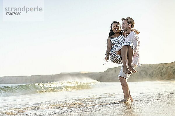 Ein junger Mann trägt seine geliebte Frau am Strand bei Sonnenuntergang an der Algarve  Portugal  Europa