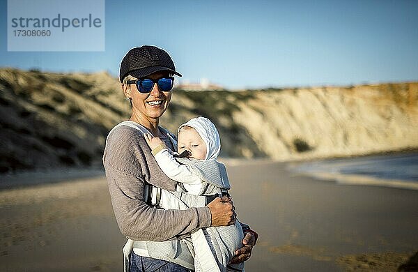 Eine Mutter mit ihrem Sohn in der Trage am Strand in Portugal