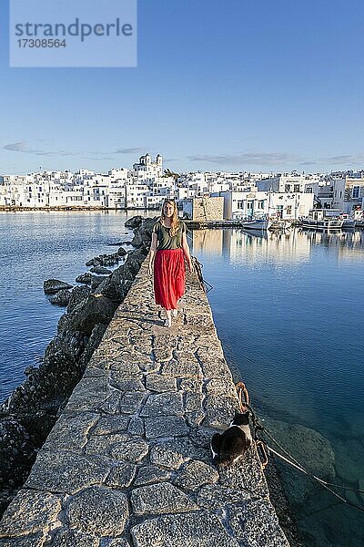 Junge Frau mit rotem Kleid auf Hafenmauer  hinten Kirche von Naoussa  Hafenstadt Naoussa  Insel Paros  Kykladen  Griechenland  Europa