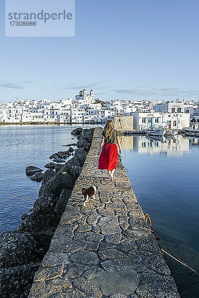 Katze und junge Frau mit rotem Kleid auf Hafenmauer  hinten Kirche von Naoussa  Hafenstadt Naoussa  Insel Paros  Kykladen  Griechenland  Europa