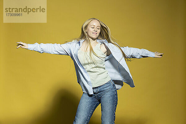 Unbekümmerte junge Frau tanzt auf gelbem Hintergrund