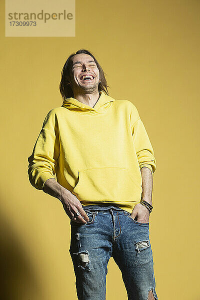 Glücklicher Mann in Jeans und Kapuzenpulli lachend gegen gelben Hintergrund