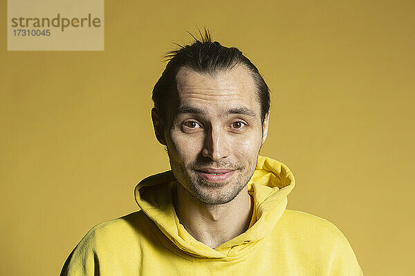 Porträt lächelnder Mann in Kapuzenpulli auf gelbem Hintergrund