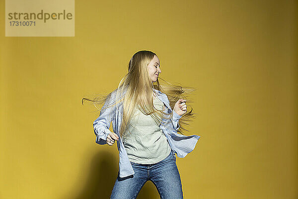 Unbeschwerte junge Frau tanzen gegen gelben Hintergrund