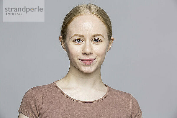 Porträt selbstbewusst lächelnde junge Frau auf grauem Hintergrund