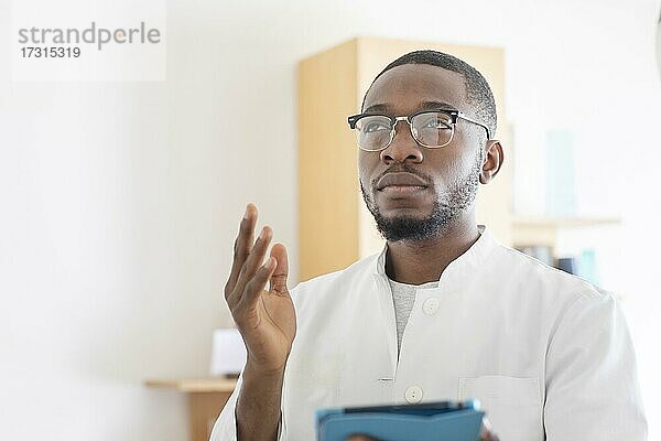 Junger schwarzer Arzt mit Kittel und Tablet erklärt in der Praxis  Freiburg  Baden-Württemberg  Deutschland  Europa