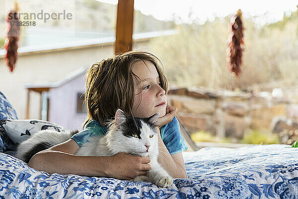 Junge liegt auf einem Bett im Freien und streichelt eine Hauskatze