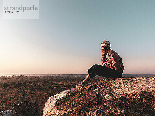 Eine Frau sitzt auf einem Felsen und beobachtet den Sonnenaufgang von einem Aussichtspunkt