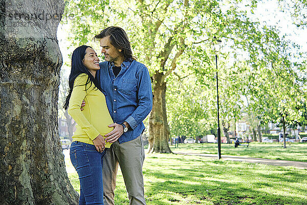 Lächelnde schwangere Frau  die ihren Mann an einem Baumstamm betrachtet