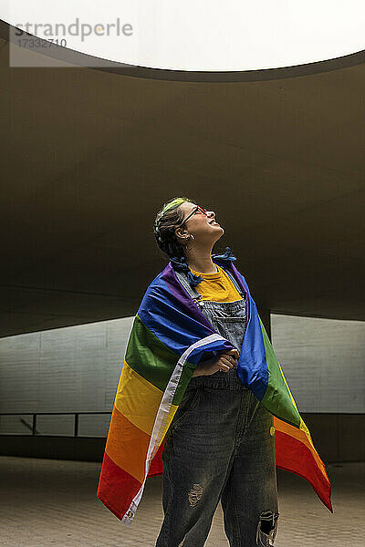 Hipster-Frau mit Regenbogenfahne  die nach oben schaut  während sie im Freien steht