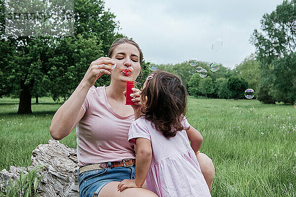 Verspielte Mutter  die mit ihrer Tochter im Park Seifenblasen bläst
