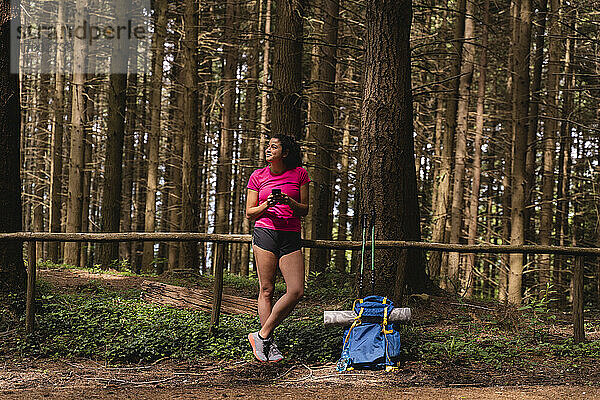 Weibliche Wanderin schaut weg  während sie ihr Handy vor den Bäumen im Wald hält