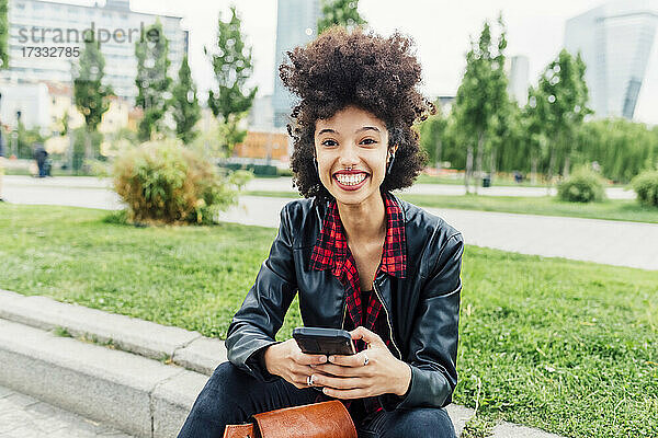 Lächelnde Frau mit Mobiltelefon im Park sitzend